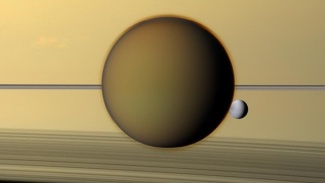 Titan nähtynä Saturnuksen pintaa vasten, mukana myös pienempi kuu Dione